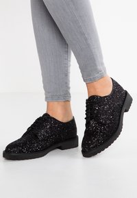 Chaussures Oxford à paillettes noires avec une semelle en caoutchouc plate et un design à lacets. La surface est entièrement recouverte de sequins noirs brillants, ajoutant de la texture.