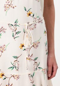 Rochie florală ușoară cu un fundal crem, având flori roz și galbene, frunze verzi și un detaliu cu talie legată.