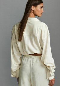 Cremefarvet oversized bluse med lange ærmer, der har en bagsideventil og glat tekstur, parret med matchende bukser med elastisk talje.