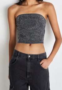 Svart denimtopp utan axelremmar med silverfärgade nitar, kort design och smal passform, kombinerad med högmidjade svarta denimbyxor.