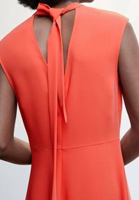 Oranges ärmelloses Kleid mit einer Schleifenbindung am Rücken. Glattes Material mit schlichter Form und subtiler Konturierung an der Taille.