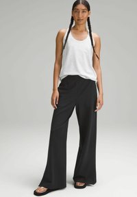 Black wide-leg pants with an elastic waistband paired with a light grey tank top. Smooth fabric and relaxed fit. Features braided hair and sandals.