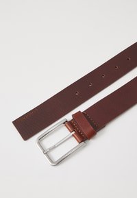 Ceinture en cuir marron avec une finition texturée, boucle en métal argenté et couture visible. Plusieurs trous d'ajustement le long de la sangle.