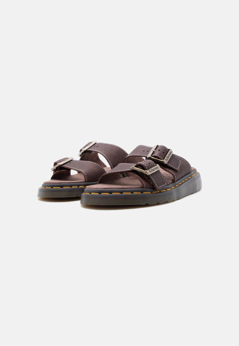 Sandali slip-on in pelle marrone con due cinturini regolabili con fibbia e suole spesse in gomma testurizzata, mostrati su uno sfondo chiaro e semplice.
