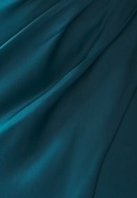 Teal stof met een gladde, licht glanzende textuur. Het materiaal valt soepel met zachte plooien en subtiele lichtreflecties op het oppervlak.