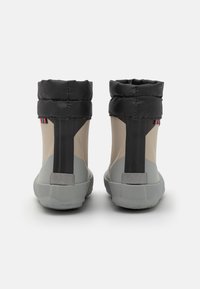 Une paire de bottes de cheville imperméables présentant une palette de couleurs grise et beige, un col rembourré noir et une semelle en caoutchouc texturée. Détail d'accent rayé.