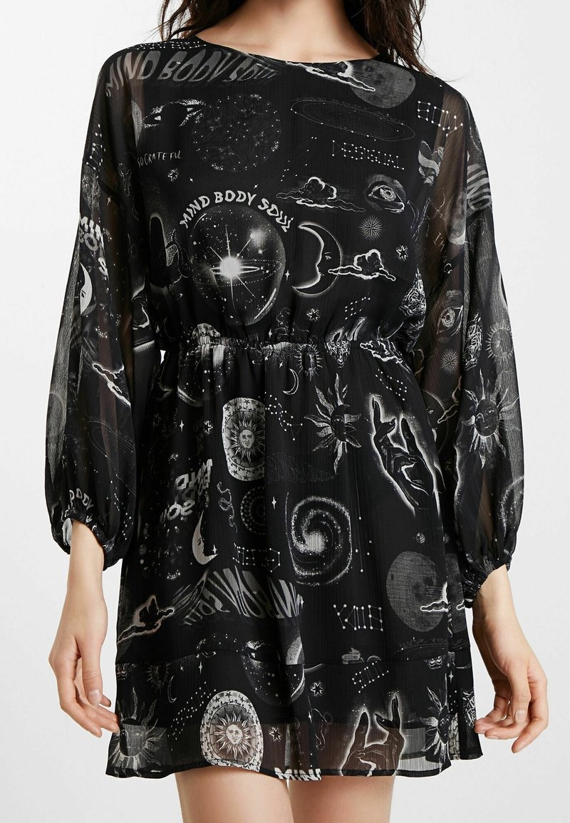 Robe noire transparente à manches longues avec des motifs psychédéliques blancs de corps célestes, d'yeux, de mains et les mots "Mind Body Soul."