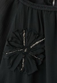 Tela negra con un diseño de flores texturizado adornado con pequeñas cuentas de plata, que muestra pétalos en capas y material ribeteado fino.