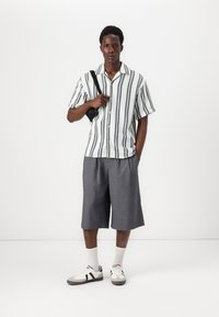 Short-sleeve striped shirt in white and navy, paired with gray knee-length shorts. White sneakers with black accents and socks complete the outfit.