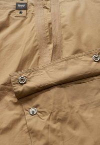 Tessuto leggero color tan con una texture liscia, caratterizzato da una chiusura a scatto, una tracolla in tessuto e dettagli in grommet. Design semplice con dettagli minimi.