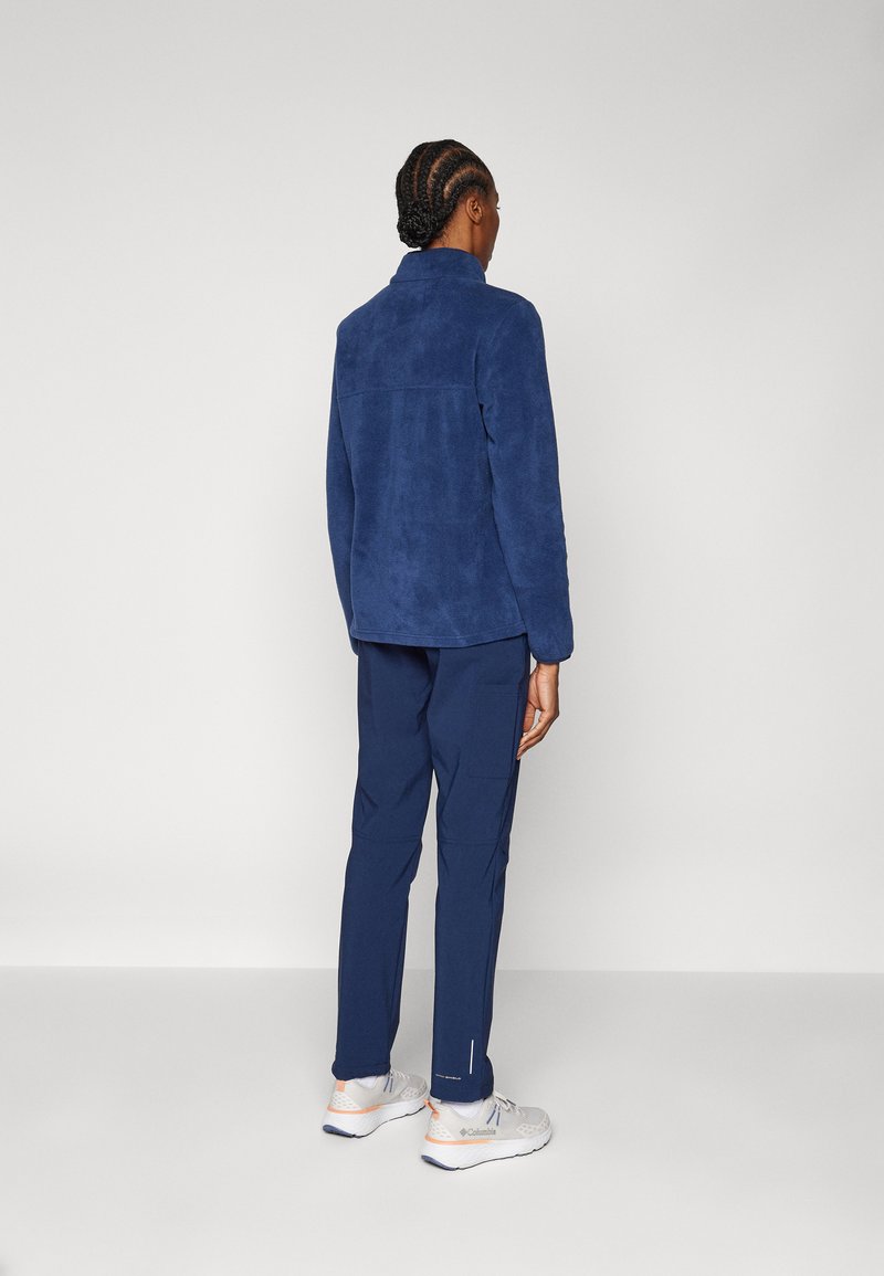 Veste en polaire marine avec une finition texturée et un col, associée à un pantalon marine et des chaussures de sport gris clair. Design minimaliste, sans motifs.