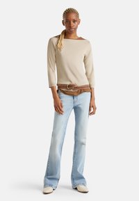 Beige pletený top s tříčtvrtečními rukávy, kombinovaný s světle modrými rozšířenými džíny. Hnědý opasek s kulatou sponou zvýrazňuje pas.