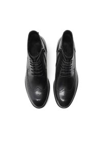 Scarpe eleganti in pelle nera con punta rotonda, dettagli perforati, lacci frontali e cerniere laterali. Texture liscia e design elegante.