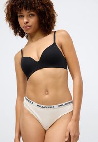 Reggiseno nero senza cuciture con spalline regolabili abbinato a slip bikini crema con fascia logo nera. Tessuto morbido, design minimalista.