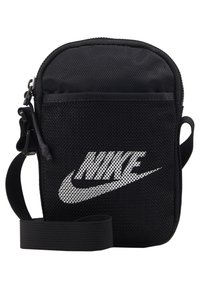 Geantă neagră din plasă tip crossbody cu închidere cu fermoar, având un logo alb Nike proeminent. Include o curea detasabilă pentru versatilitate.