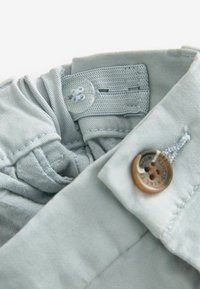 Primo piano della cintura di pantaloni grigio chiaro con banda elastica regolabile cucita con bottone e un bottone marrone a quattro fori sul tessuto esterno.
