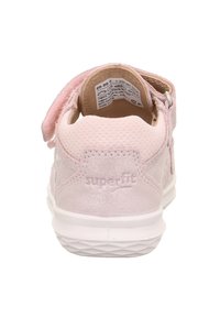 Lys rosa sneaker med en blød, tekstureret overdel og en velcro-rem. Har en hvid sål og "superfit" branding bagpå.
