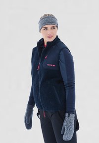 Mørkeblå fleece vest med højt krave, lynl�åslommer og røde detaljer; bæres over en langærmet bluse. Grå mønstrede vanter fuldender outfittet.