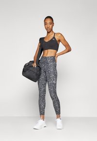 Fekete sportmelltartó, szürke terepmintás leggings, fehér sportcipők és fekete edzőtáska. Főbb jellemzők: testhezálló fazon és kontrasztos minták.
