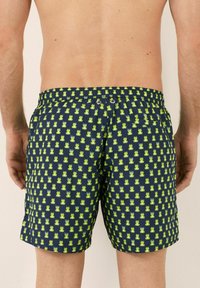 Pantaloni da mare con una base blu scuro caratterizzati da un motivo ripetuto di rane verdi. Vita elastica, senza hardware visibile, lunghezza sopra il ginocchio.