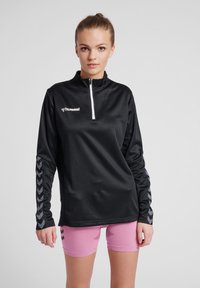 Zwart lange mouwen sporttop met een kwart rits en chevronpatroon op de mouwen, gemaakt van textuurmateriaal. Hummel-logo op de borst.