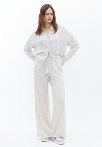 Lichte, gestreepte button-up shirt in wit en blauw, gecombineerd met losse, crèmekleurige broeken. Beide kledingstukken hebben een relaxte pasvorm en een zachte textuur.