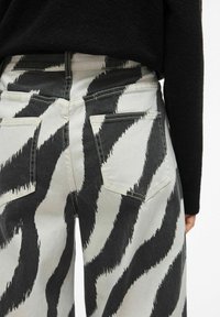 Dżinsy w czarno-białe paski zebra z wysokim stanem, tylnymi kieszeniami i teksturowanym denimem. Minimalistyczny design z kontrastującymi kolorami.