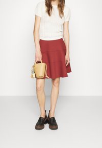 Suéter blanco de punto con mangas cortas, falda roja acampanada, mocasines negros y un pequeño bolso marrón claro con un charm decorativo.