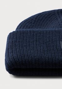 Cappello beanie a coste blu scuro ripiegato sul bordo su una superficie bianca.