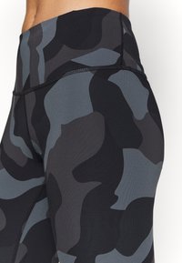 Höga leggings i ett kamouflage-mönster med nyanser av svart och grått, tillverkade av stretchigt, fukttransporterande tyg med flatlock-sömmar.