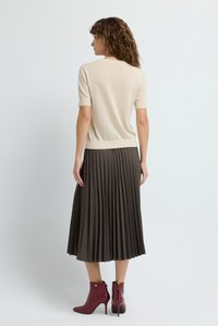 Hellbeige kurzärmliger Pullover, kombiniert mit einem braunen Faltenrock und burgunderroten Ankle Boots. Weiche Textur, schlanke Form und minimalistisches Design.