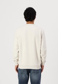 Kremfarget hettegenser med lange ermer, ribbestrikkede mansjetter og rund hals, brukt med blå jeans. Glatt tekstur, minimalt med detaljer.
