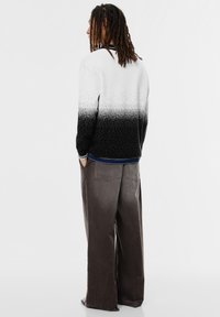 Pull à dégradé noir et blanc avec une texture à pois, manches longues et coupe décontractée, associé à un pantalon en velours côtelé gris ample.