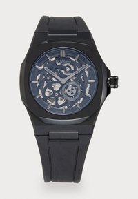 Schwarze Skelettuhr mit rundem Ziffernblatt, Gummiband, metallischen Akzenten und sichtbaren inneren Mechanismen. Verfügt über dezente Stundenmarkierungen und Zeiger.