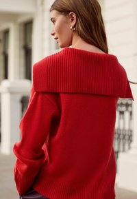 Red sweater with a wide ribbed collar and long sleeves. The texture is soft and knit, featuring a relaxed fit and detailed ribbing at the hem.