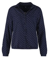 Chemise bleu marine à boutons avec motif triangulaire blanc, manches longues, deux poches poitrine et ourlet froncé. Tissu doux avec une texture lisse.