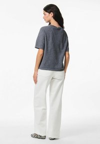 Top grigio a maniche corte in maglia con una vestibilità rilassata, abbinato a pantaloni bianchi a gamba larga e scarpe a motivi bianco e nero.
