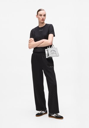 Black short-sleeve shirt with rhinestone accents, paired with black trousers featuring rhinestones. Silver handbag with logo and black sneakers.