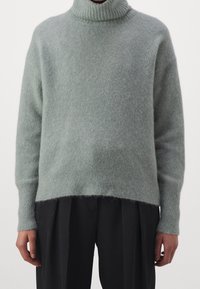 Hellgrüner, weicher Wollpullover mit Rollkragen und geripptem Saum. Verfügt über einen lockeren Schnitt und eine leicht flauschige Textur. Kombiniert mit schwarzen Hosen.