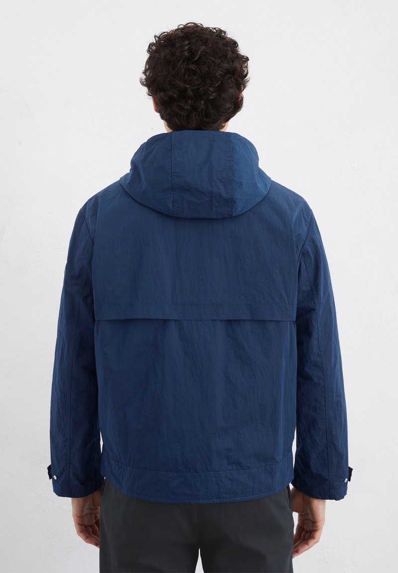 Marineblauwe lichte jas met een capuchon, voorzien van een kwartlange achterkant, rechte mouwen en een geprofileerde stof.