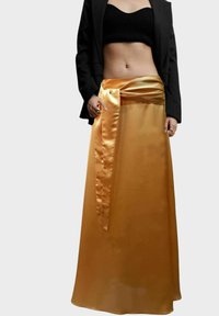 Larga falda fluida en satén dorado brillante con una cinturilla ancha y un lazo atado como acento. Combinada con una blusa negra corta y una americana.