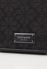 Borsa a mano in tessuto nero con motivo floreale testurizzato, dotata di una piastra in metallo argentato con il logo "kate spade NEW YORK."