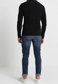 Chemise noire à manches longues avec un col rond, associée à un jean skinny bleu foncé et des baskets blanches. La chemise a une coupe ajustée et une texture douce.
