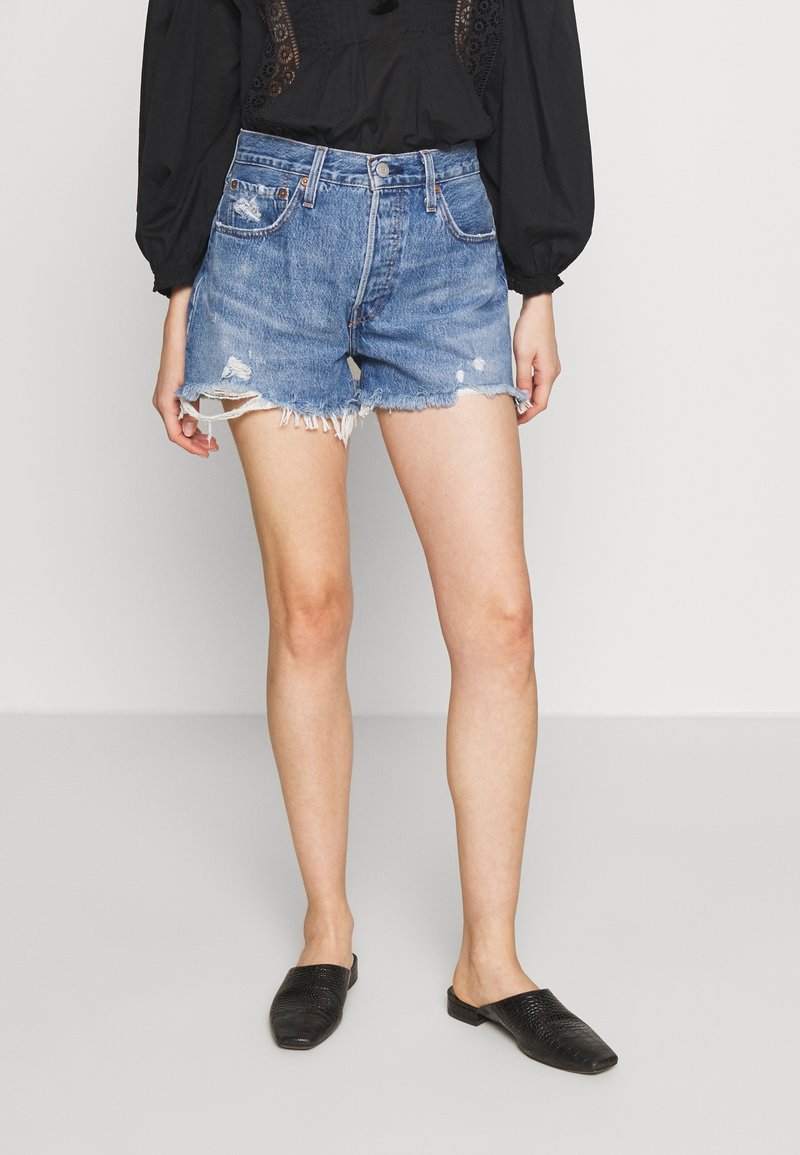 Jeansshorts med slitna kanter och fransade detaljer. Ljusblåt tyg med små hål, bärs med svarta texturerade slip-on skor.