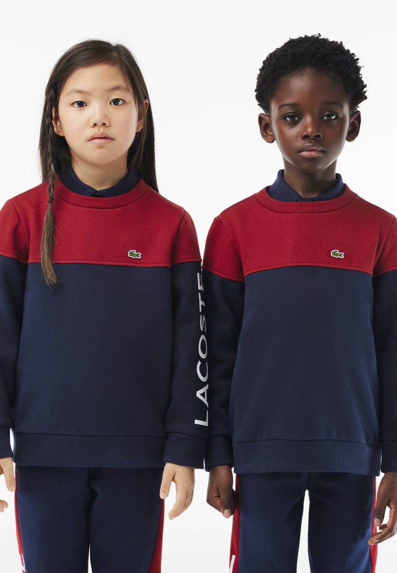 Sweatshirts rouges et bleus marine à col rond avec logo sur la poitrine ; manches longues ; présente des couleurs contrastantes et une texture lisse.