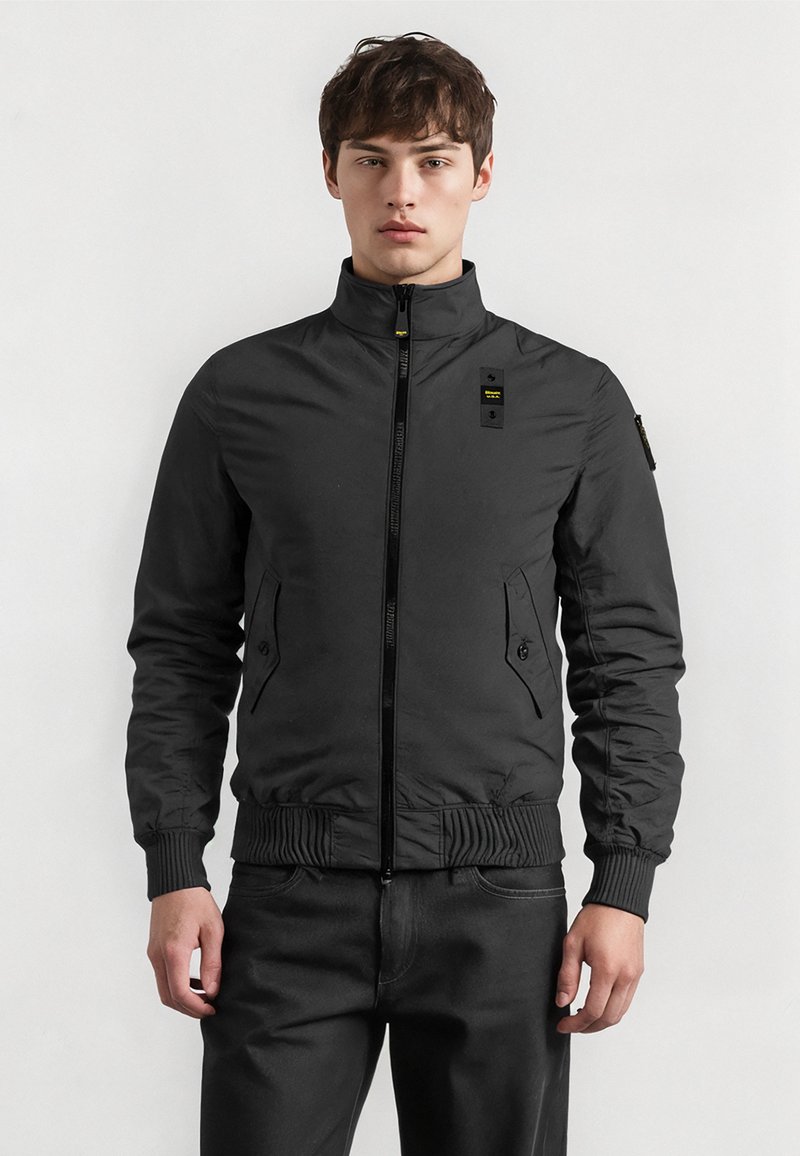 Mustat pommikonesat ovat valmistettu sileästä kankaasta, joissa on korkea kaulus, vetoketjukiinnitys, sivutaskut sekä joustavat hihansuut ja helma.