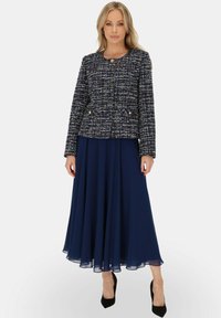 Granatowa tweedowa marynarka z złotymi guzikami, zestawiona z lejącą granatową spódnicą z chiffonu, noszona z czarnymi szpilkami.