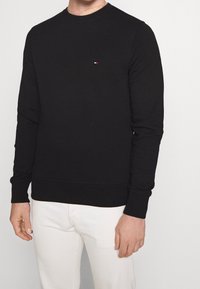Felpa nera, in misto cotone, con collo tondo e maniche lunghe, caratterizzata da un discreto ricamo del logo in rosso, bianco e blu sul petto.