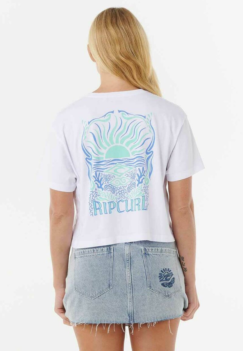 Weißes, kurzes T-Shirt mit einem bunten Grafikdruck auf der Rückseite, der Sonne, Wellen und den Text "Rip Curl" zeigt. Darunter ein distressed Denim-Rock.