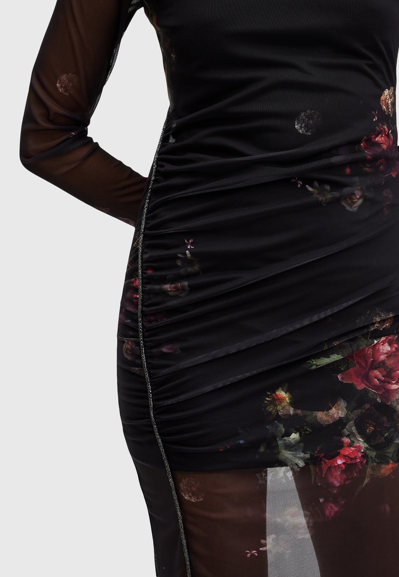 Vestido negro con diseño arrugado, acentos de estampado floral, mangas de tul transparente y detalle de cremallera plateada a lo largo del costado.